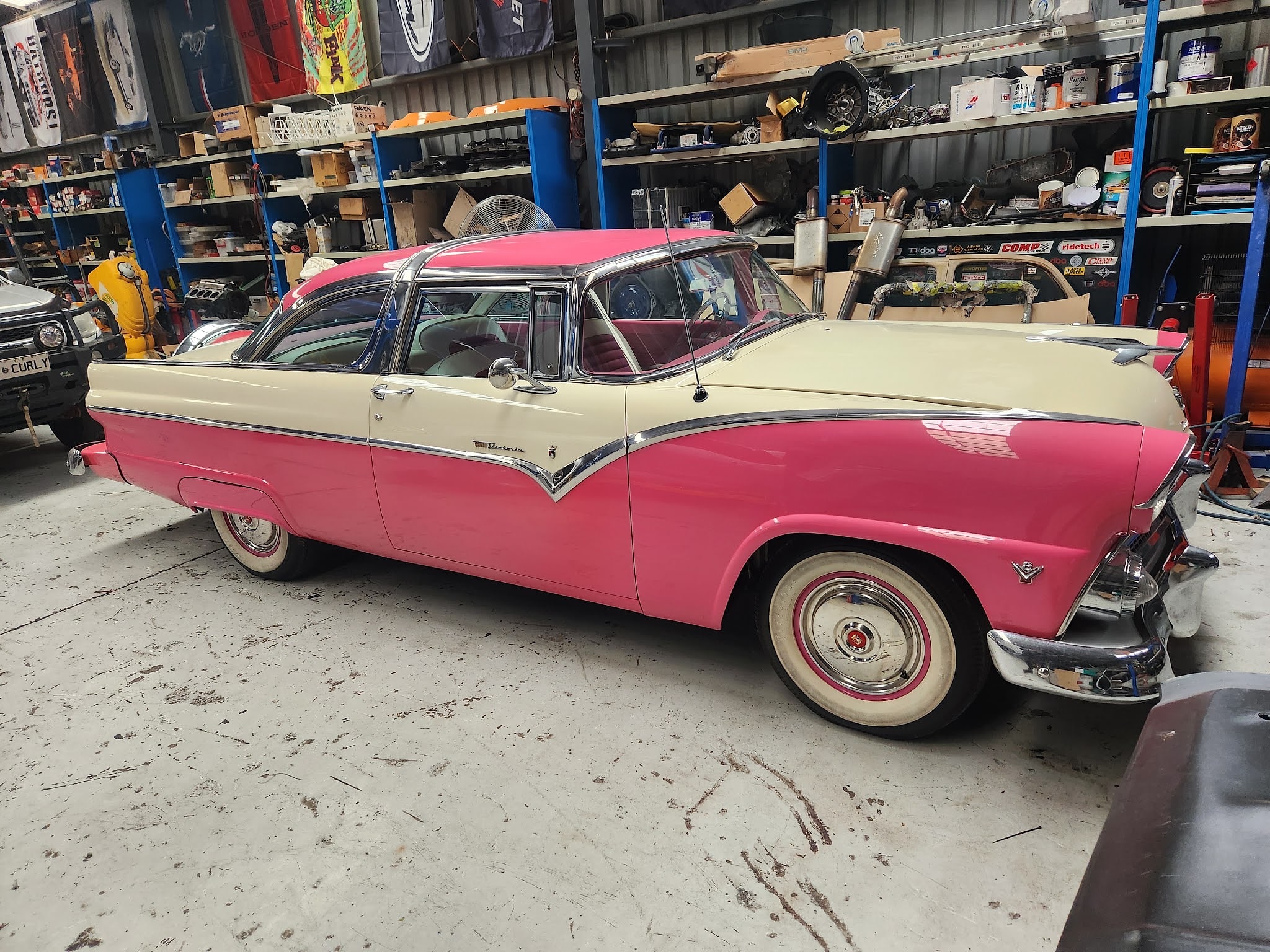 A Ford Crown Victoria in hot pink and cream with full chrome trim and whitewall tyres, inside the workshop