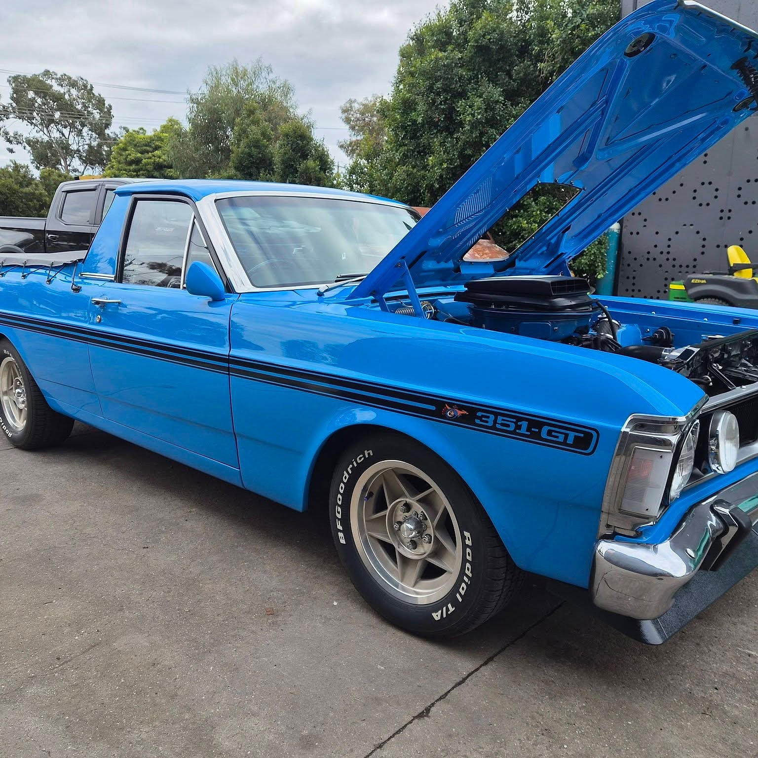A blue Ford Falcon GT ute side on with the bonnet up, sitting on polished five spoke wheels