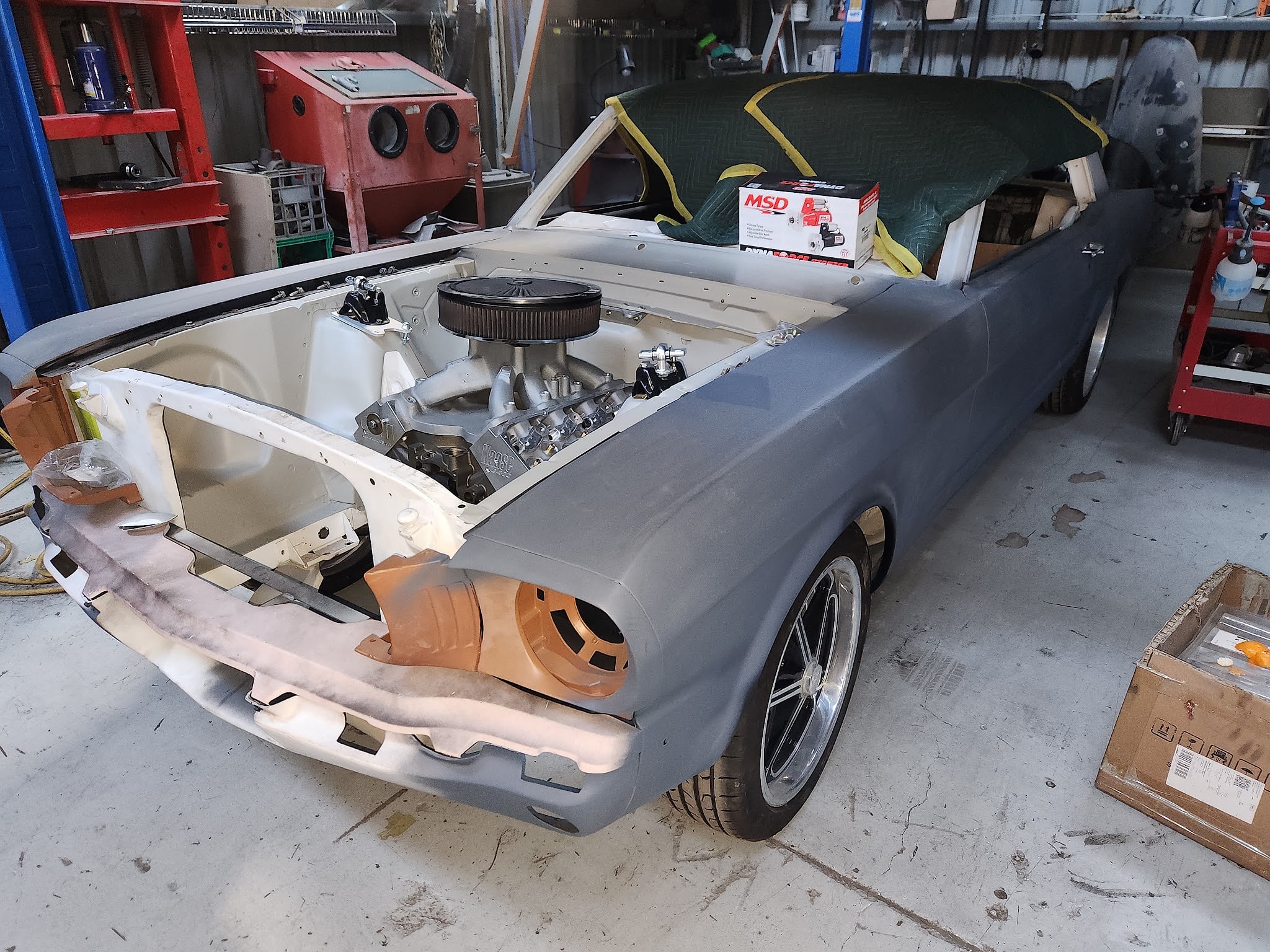 A first generation Mustang convertible part way through a restoration, one guard in grey primer and a fresh V8 already in the engine bay