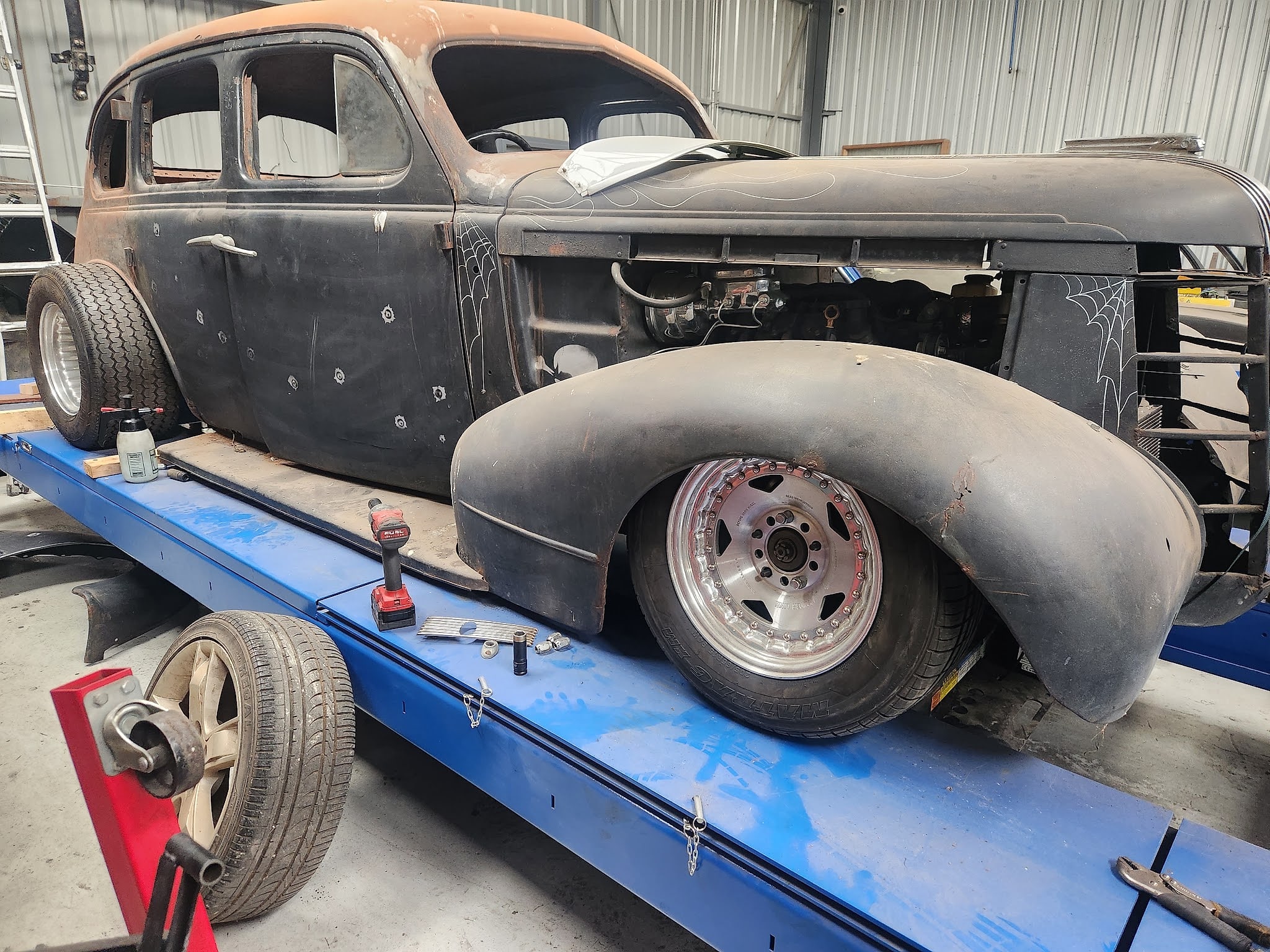 A 1930s sedan hot rod up on the four post heavy duty hoist, satin black with hand pinstriped spiderwebs on the guards