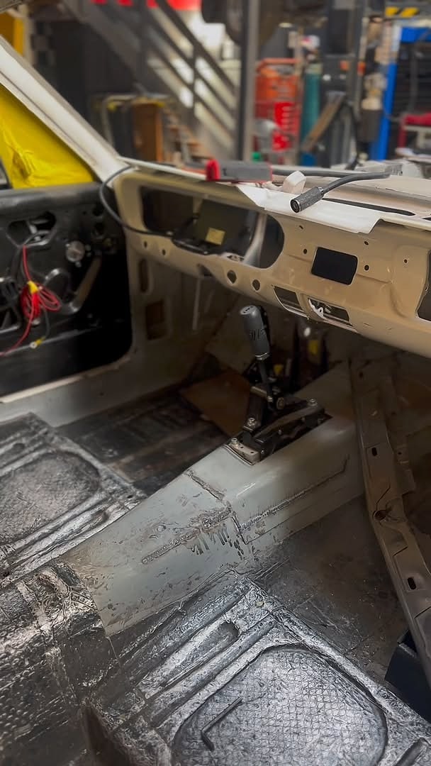The inside of a car shell stripped back, floor pan bare with new sound deadening laid in and the dash shell in primer